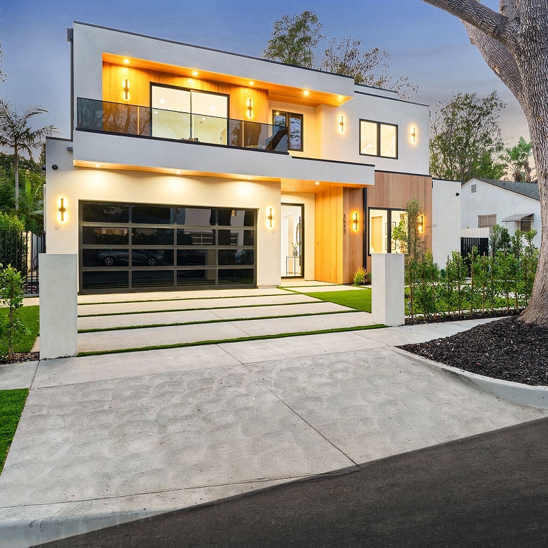 Maison moderne (3507) blanche et bois, deux étages. Garage vitré noir, allée design béton/gazon, éclairage extérieur chaleureux au crépuscule.